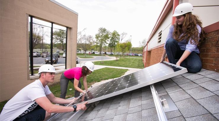 Three students in hard hats working on a solar panel